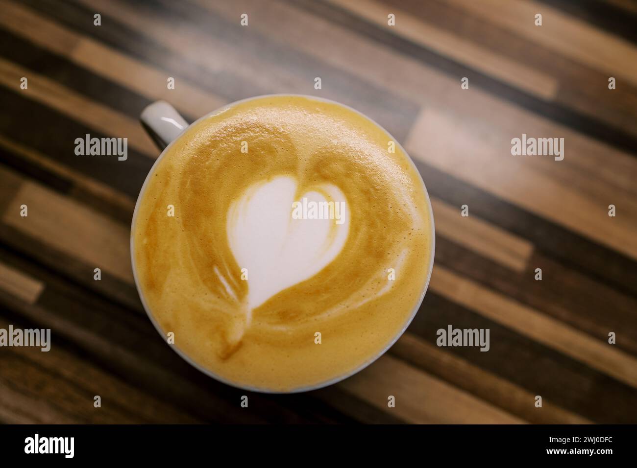 Cappuccino with a heart on the foam stands in a cup on a wooden table. Top view Stock Photo