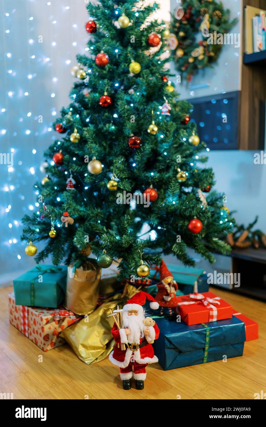 Santa and elves figurines near colorful gifts lying on the floor under the Christmas tree Stock Photo
