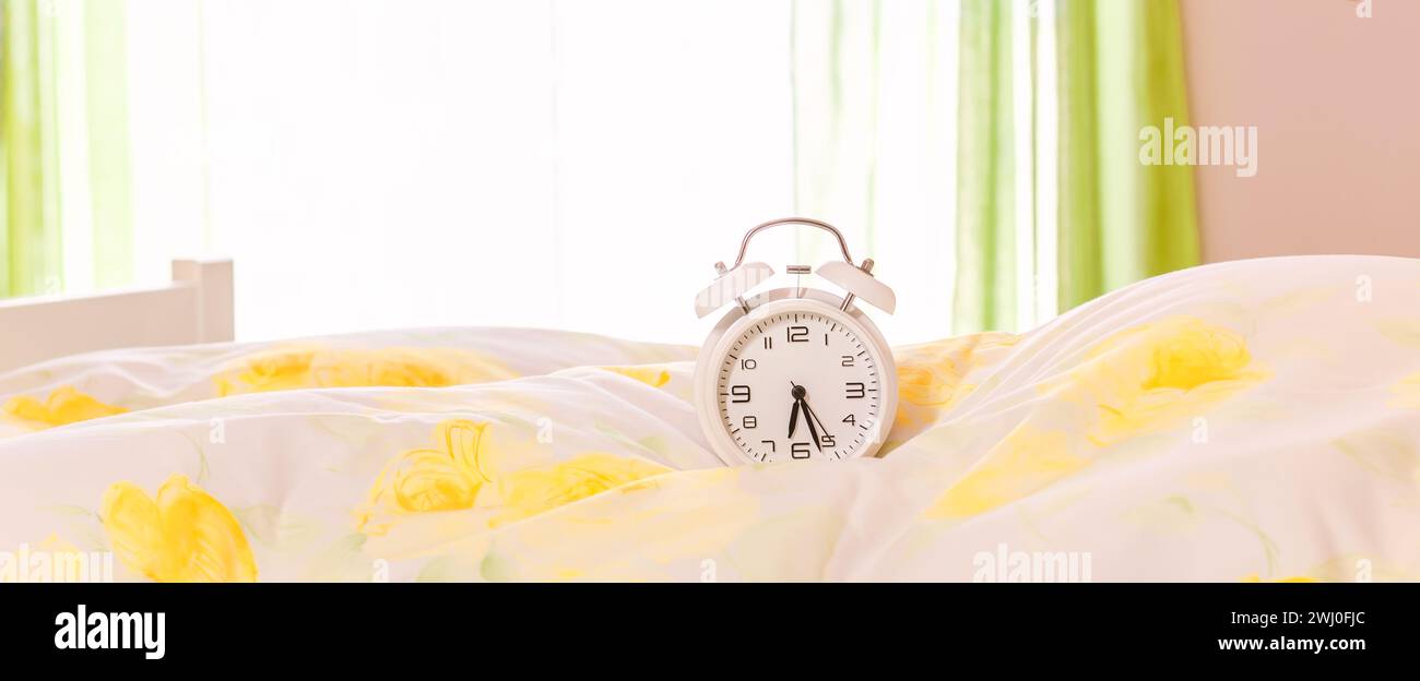 Clock on the bed. Alarm clock on the duvet, pillow. Advertising concept, copy space. web Banner Stock Photo