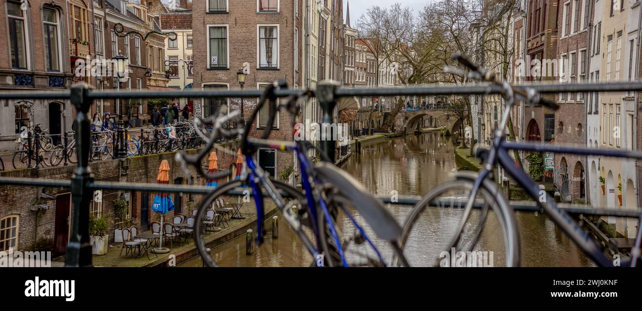Key locked bikes to bridge railing with canal behind of historic Dutch city center with shops along the wharf a level above the waterway Stock Photo