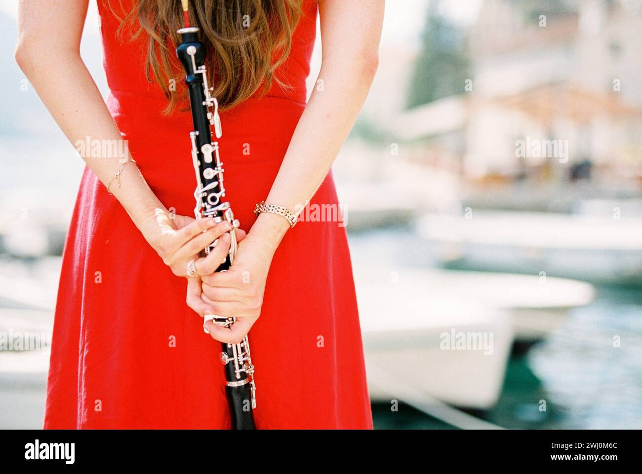 Girl-musician with a clarinet in her hands behind her back stands at the pier. Cropped. Back view Stock Photo