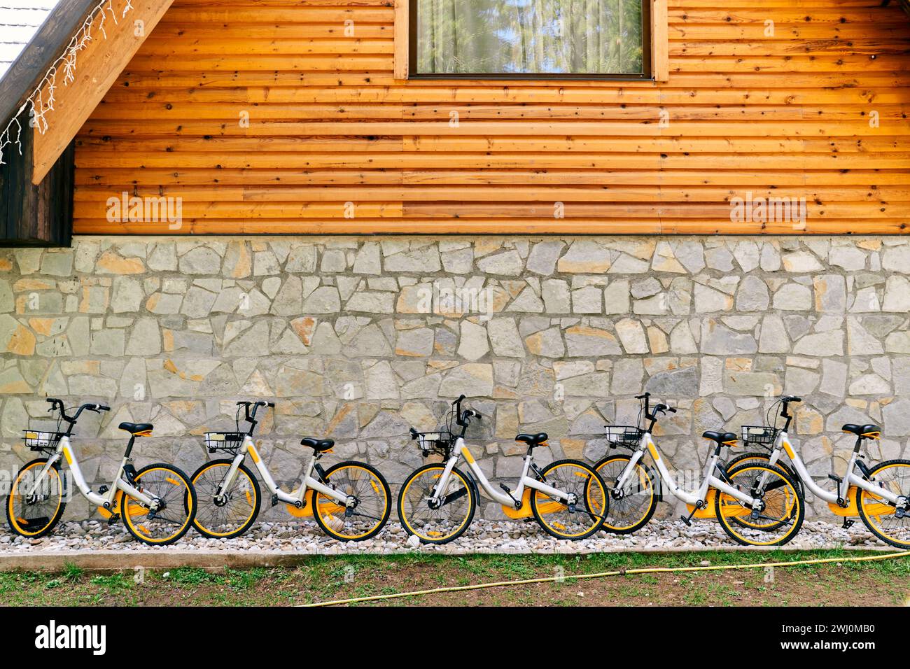 Row of colorful two-wheeled bicycles with baskets stands against the wall of a house Stock Photo