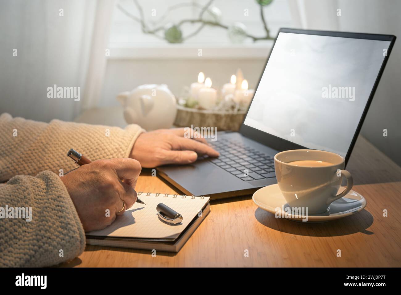 Hands of an older woman using laptop on a budget online shopping for Christmas presents and making notes on a table with advent Stock Photo