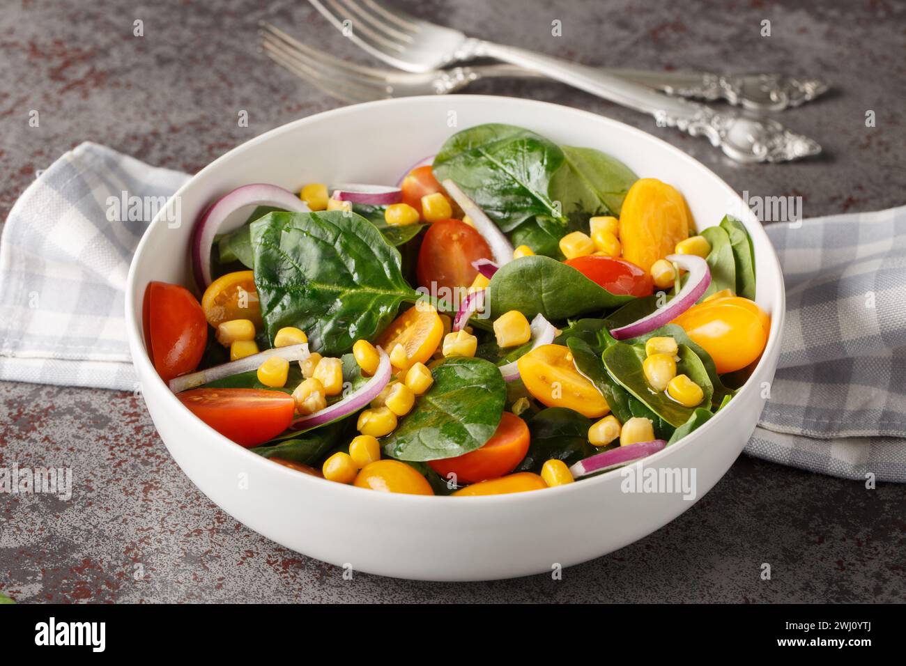 Light simple salad of fresh spinach, corn, cherry tomatoes and red onions with olive oil dressing close up in a bowl on the table. Horizontal Stock Photo