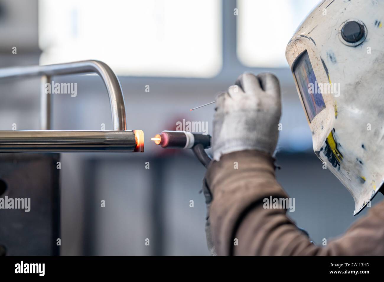 A man wearing a welding helmet is using a welding machine to weld a metal pipe Stock Photo