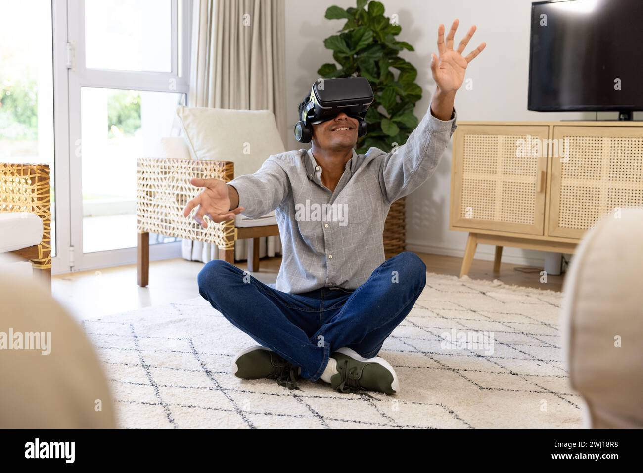 Happy biracial man using vr headset touching virtual screen at home Stock Photo