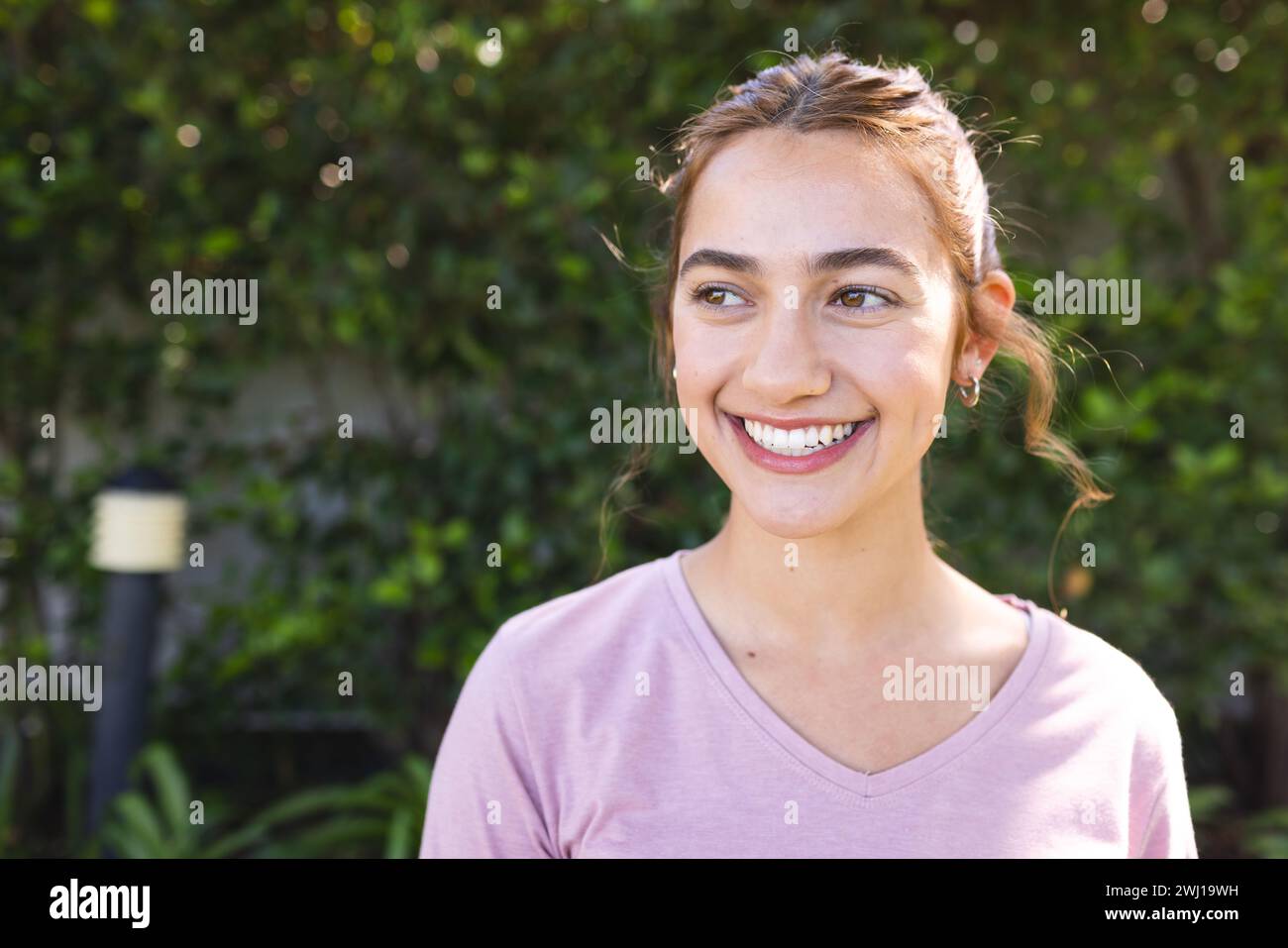 Happy biracial woman with long brown hair smiling in sunny garden, copy ...