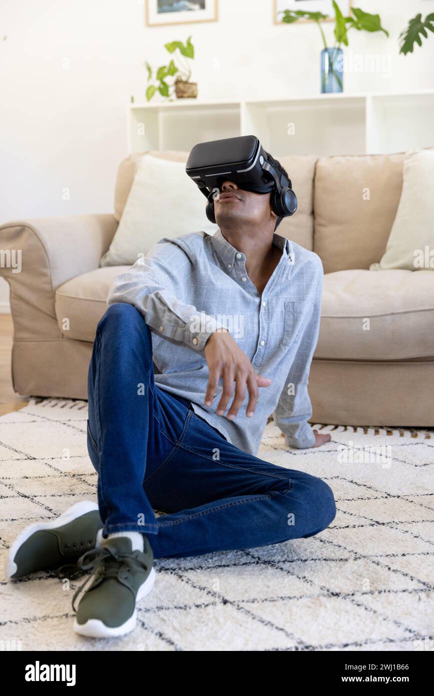 Biracial man using vr headset sitting on floor at home Stock Photo