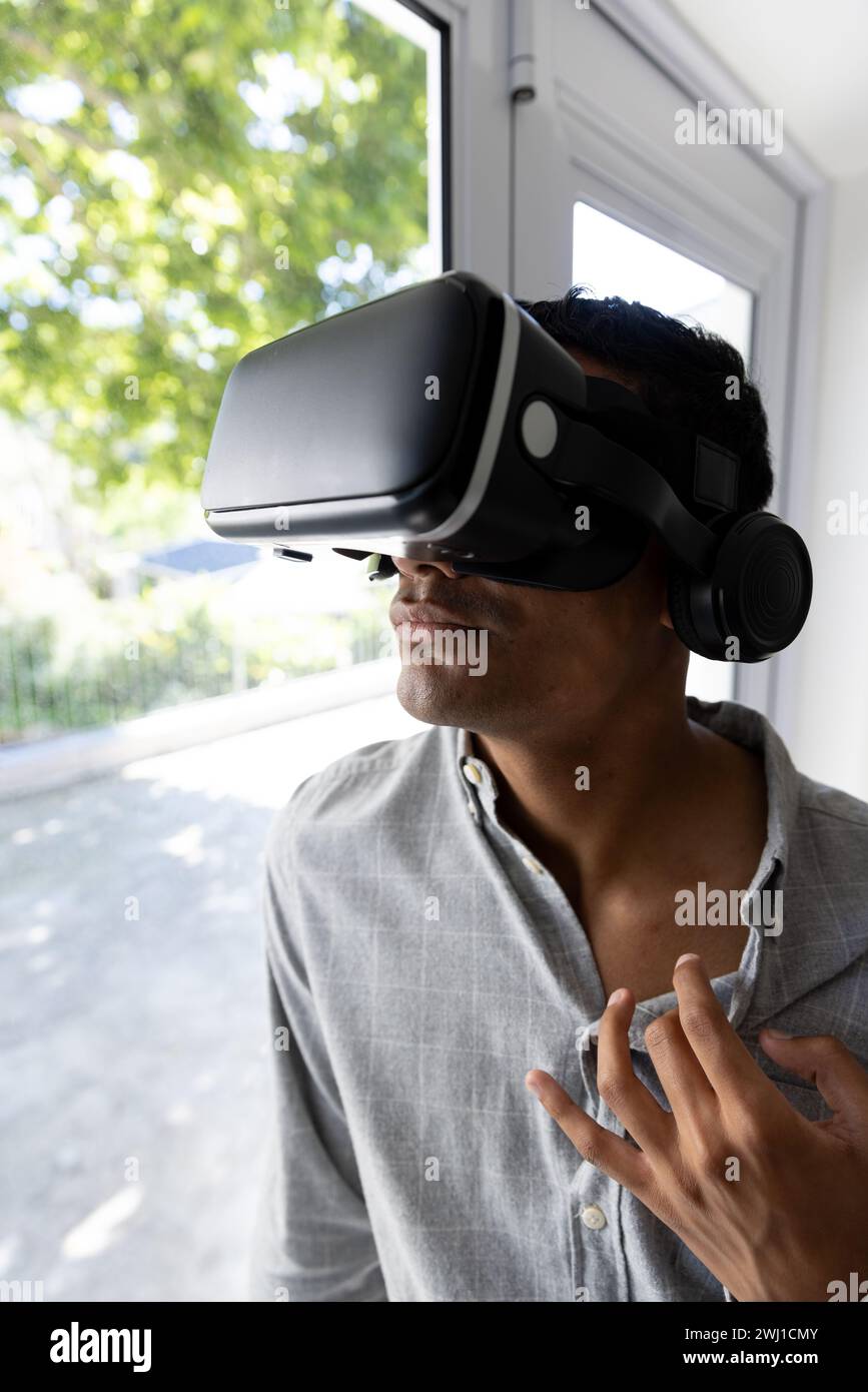 Biracial man using vr headset next to window at home Stock Photo