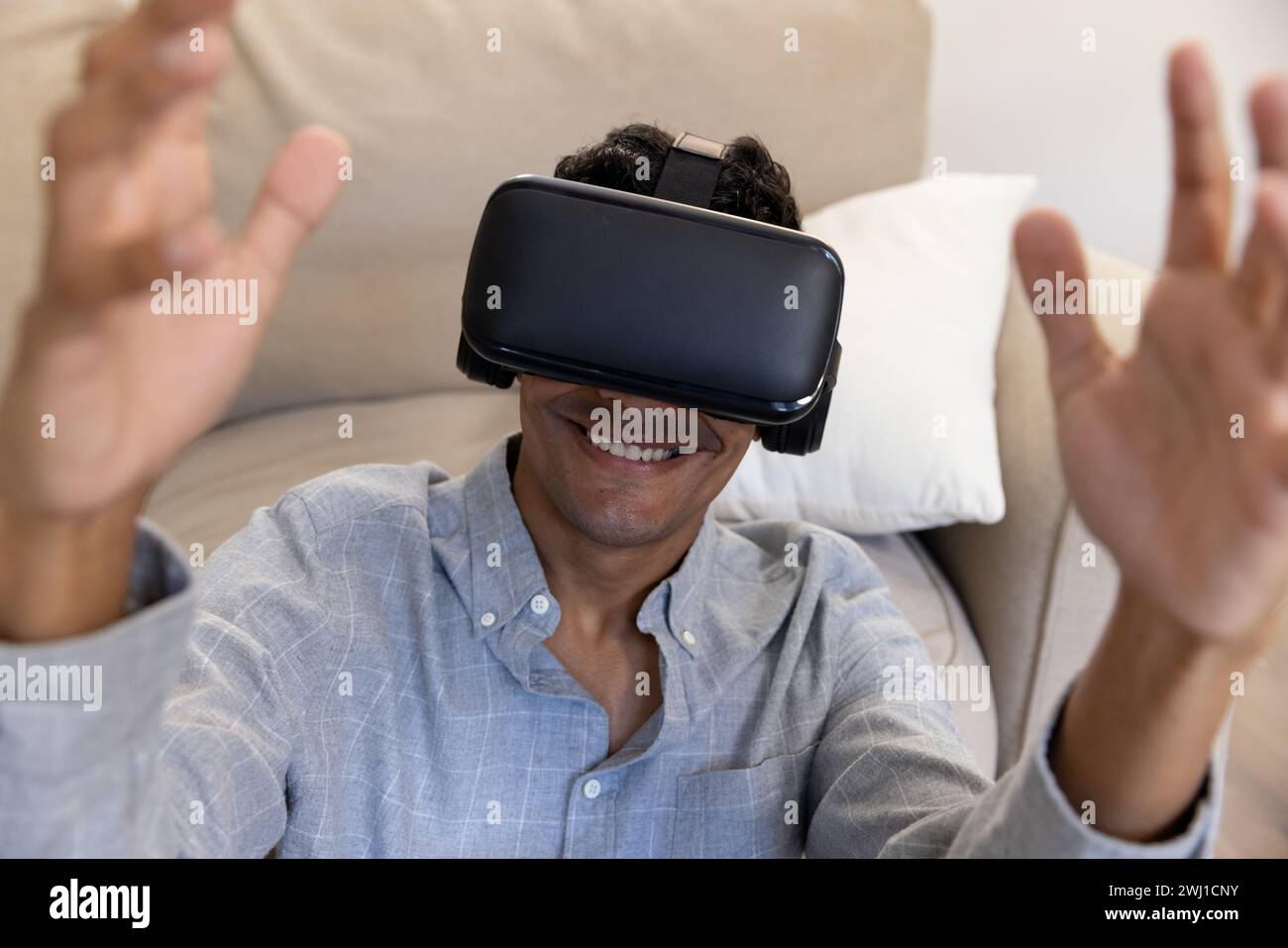 Happy biracial man using vr headset touching virtual screen at home Stock Photo