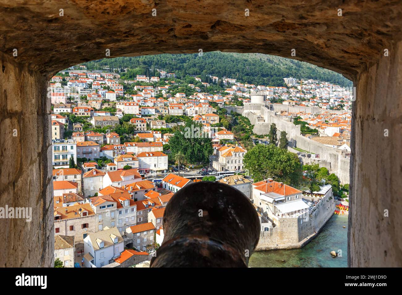 View of the old town through an opening in the wall of the fortress with a cannon in Dubrovnik, Croatia Stock Photo