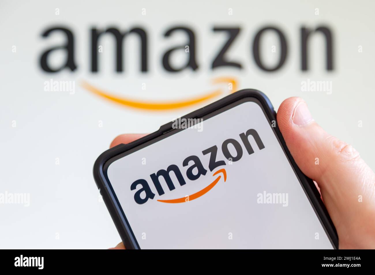 Hand holding cell phone with Amazon logo online marketplace online trading ecommerce computer screen Stock Photo