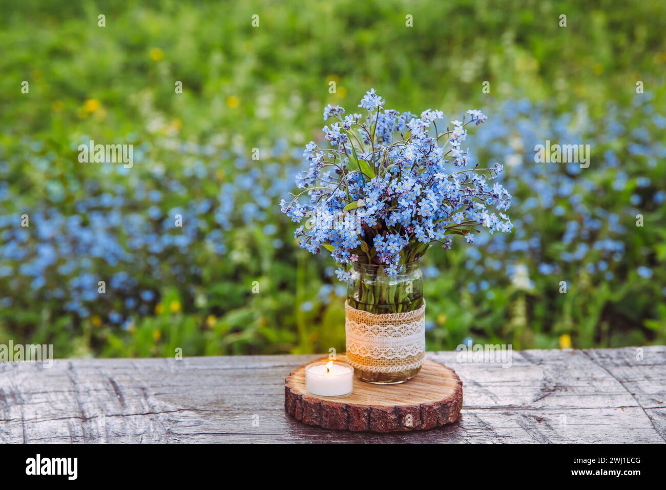 Bouquet of blue blossom wild flowers Myosotis also known as Forget me not or scorpion grasses in decorated mason jar. Beautiful vintage floral still. Stock Photo