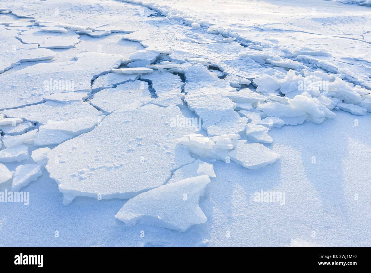 Cracked ice hummocks covered with snow. Broken ice fragments lay on the coast of frozen Baltic Sea on a winter day Stock Photo