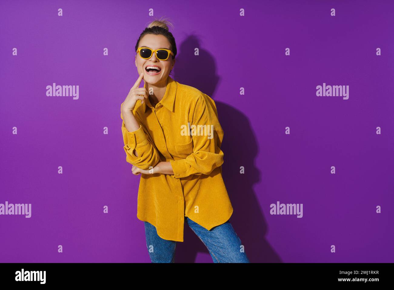 Young cheerful girl wearing yellow shirt and sunglasses against purple