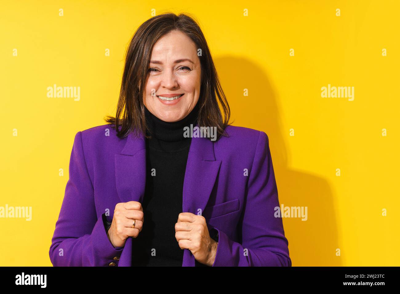Cheerful middle aged woman wearing purple blazer smiling against yellow background Stock Photo