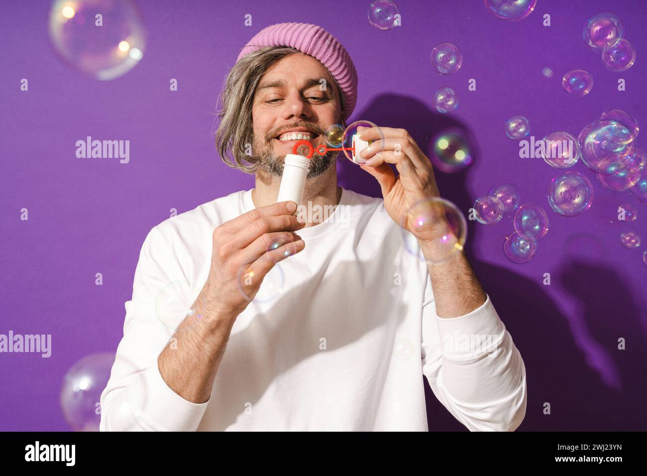 Carefree middle aged man blowing soap bubbles against purple background Stock Photo