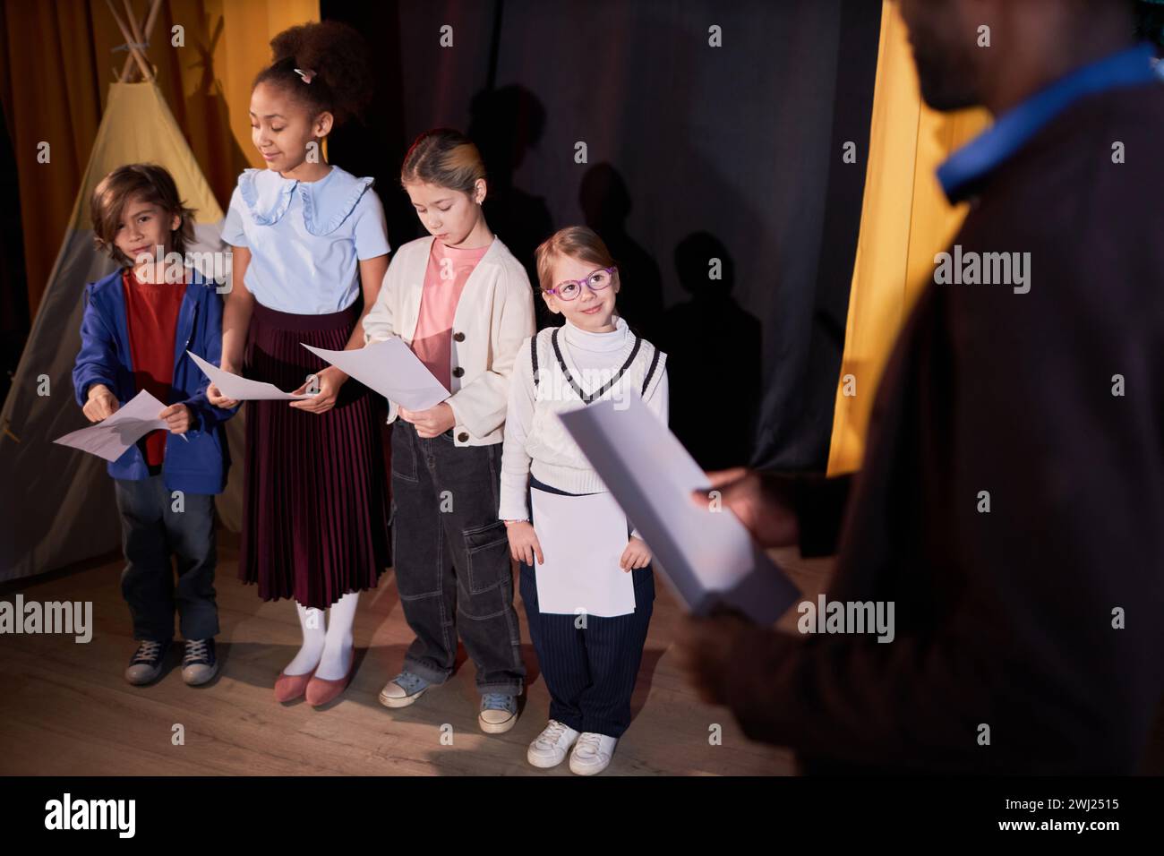 Over shoulder view of school drama teacher directing group of kids ...