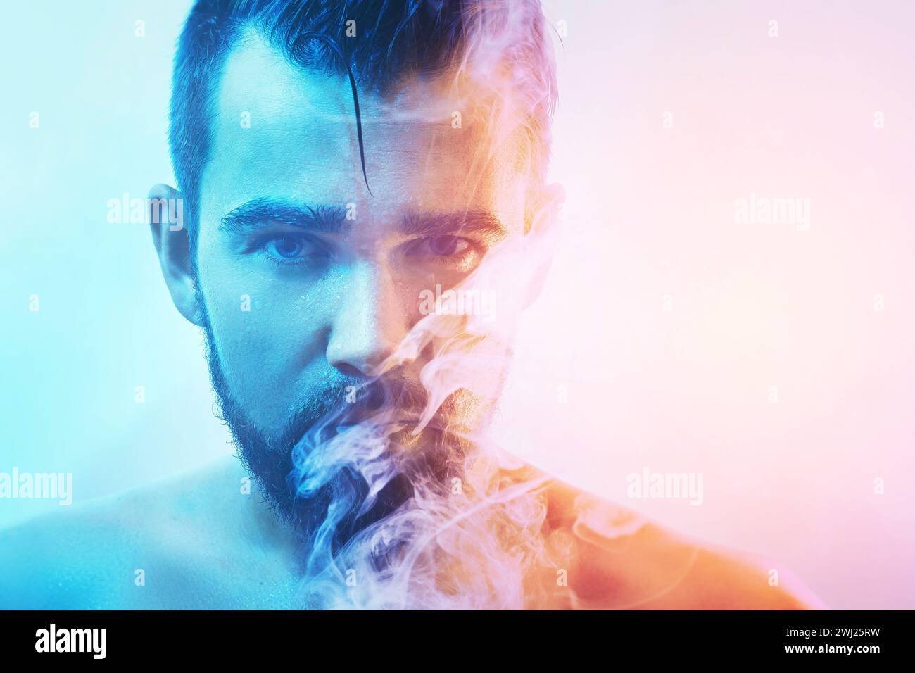 Handsome young man with wet skin in colorful light smoking cigarette or marijuana Stock Photo