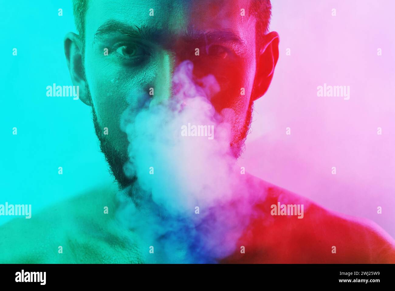 Handsome young man with wet skin in colorful light smoking cigarette or marijuana Stock Photo
