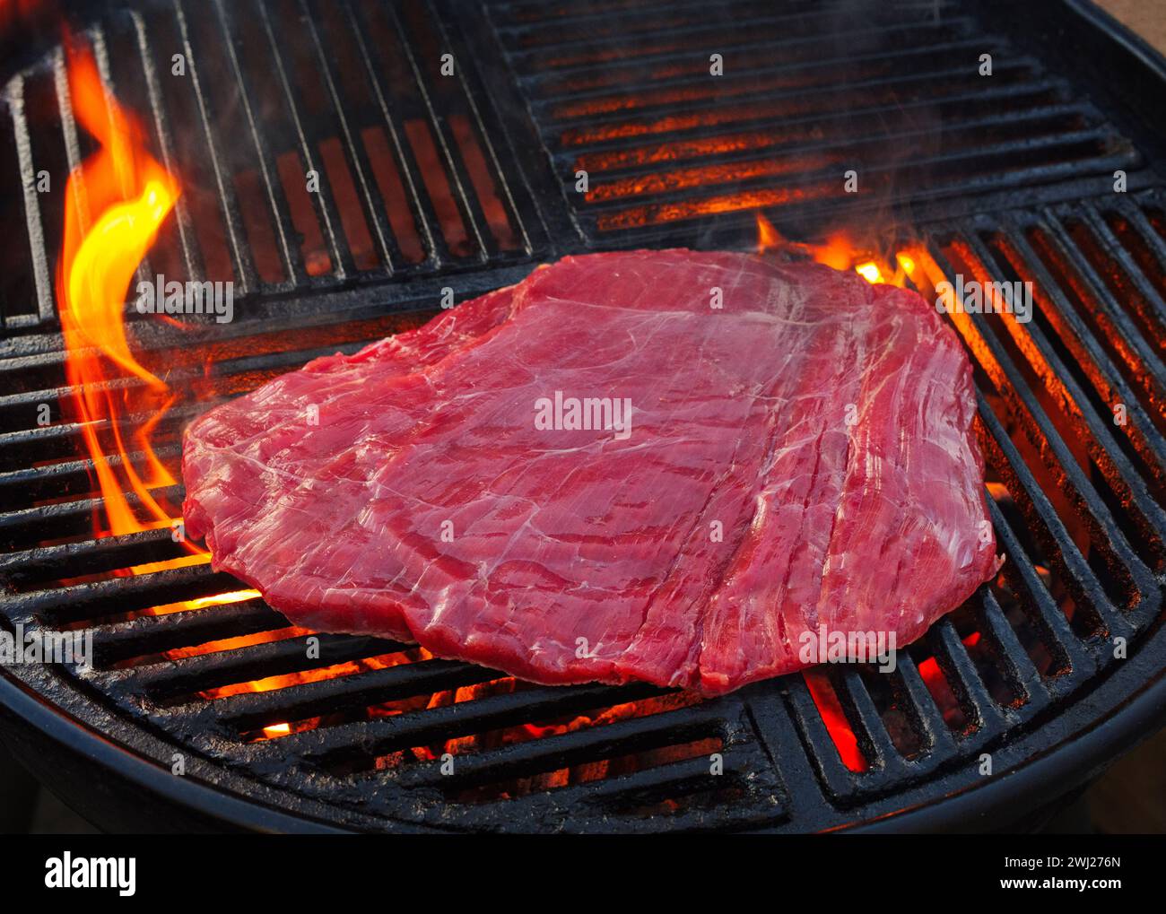 Traditional raw barbecue flanksteak steak as closeup on a charcoal grill with fire Stock Photo