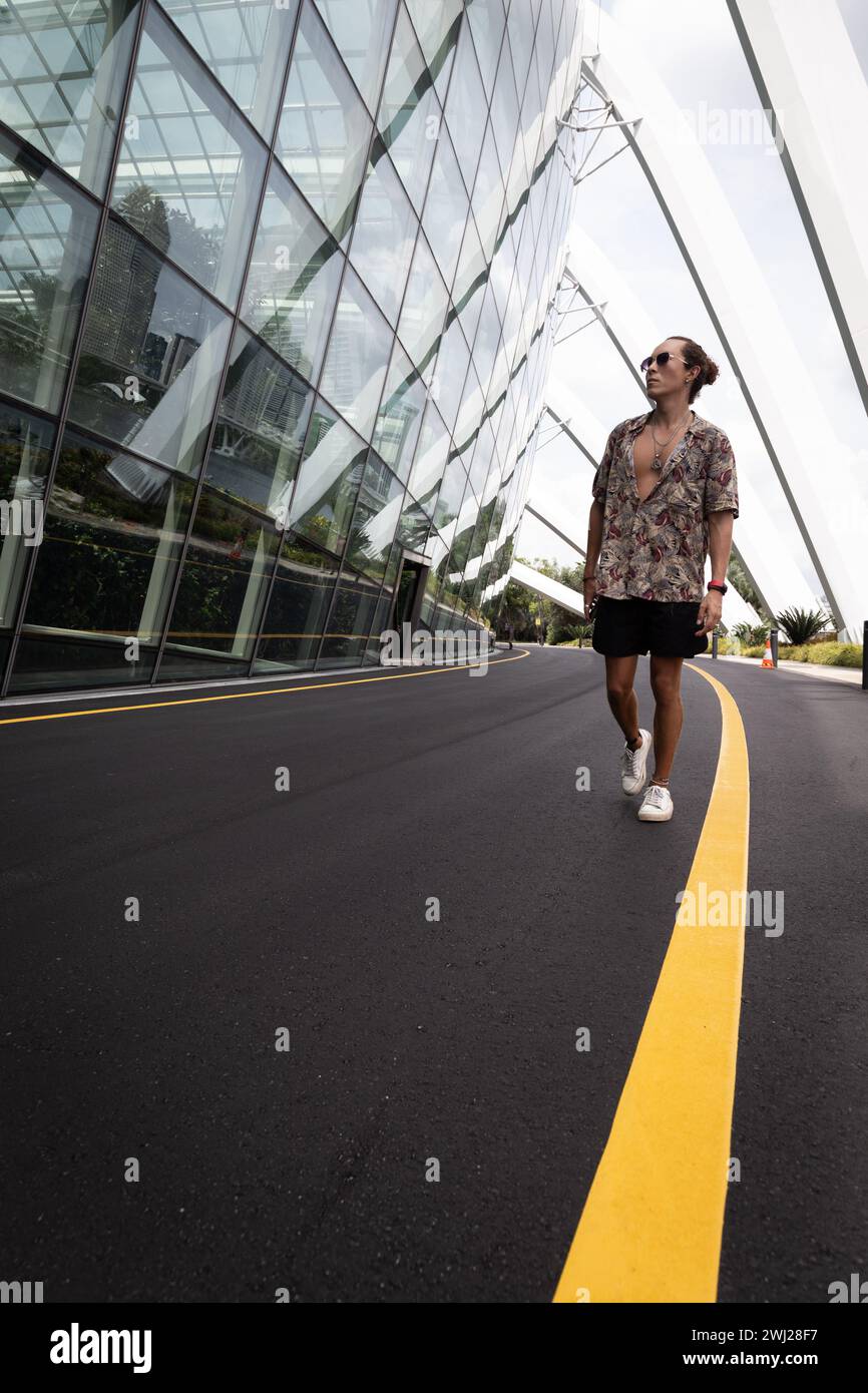 Male tourist walking on concrete road, next to modern glass building Stock Photo