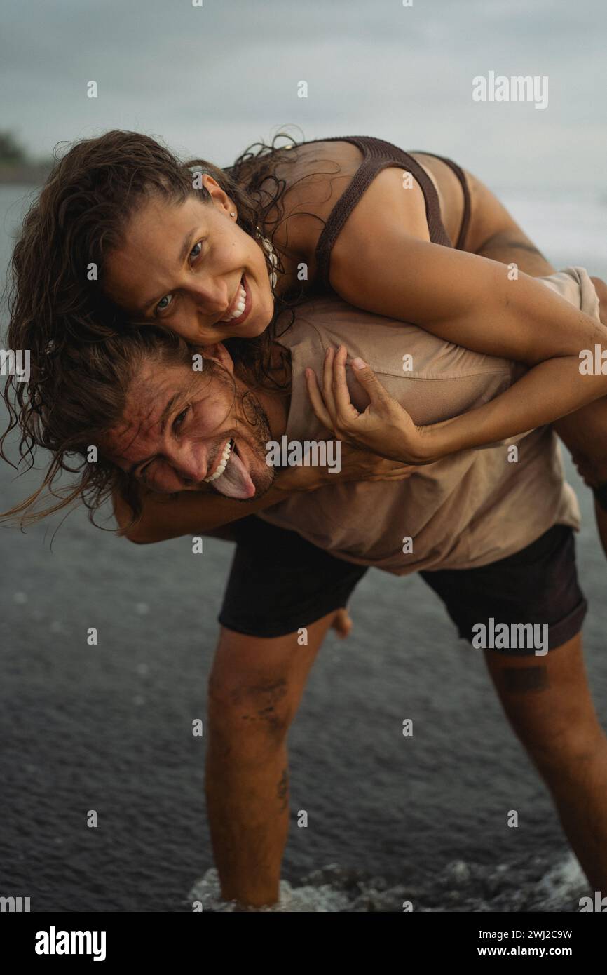 Cheerful man piggybacking woman while standing at shore Stock Photo