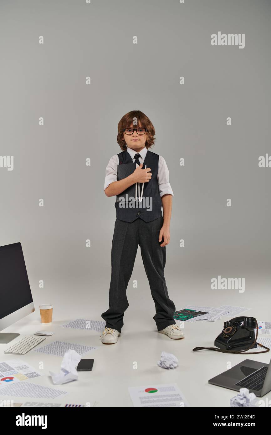 A young professional surrounded by technology and office supplies, holding notebooks on grey Stock Photo
