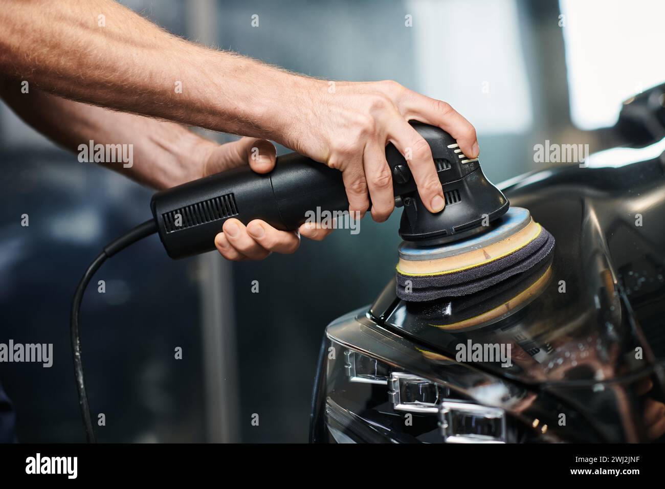 cropped view of dedicated professional using polishing machine carefully on black modern car Stock Photo