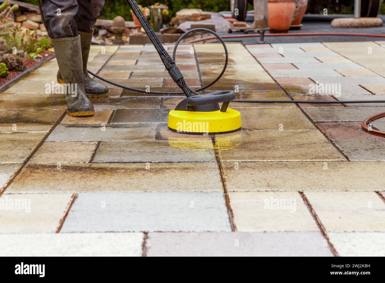 Cleaning stone slabs on patio with the highpressure cleaner. Person
