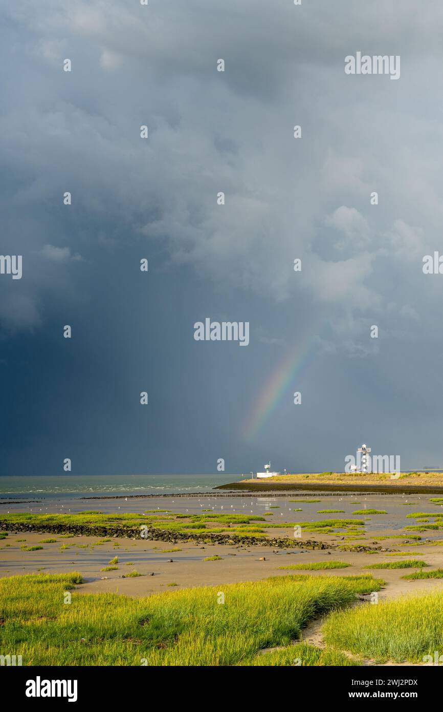 Heavy thunder clouds and a rainbow over the harbour entrance of the Dutch city of Terneuzen. Stock Photo