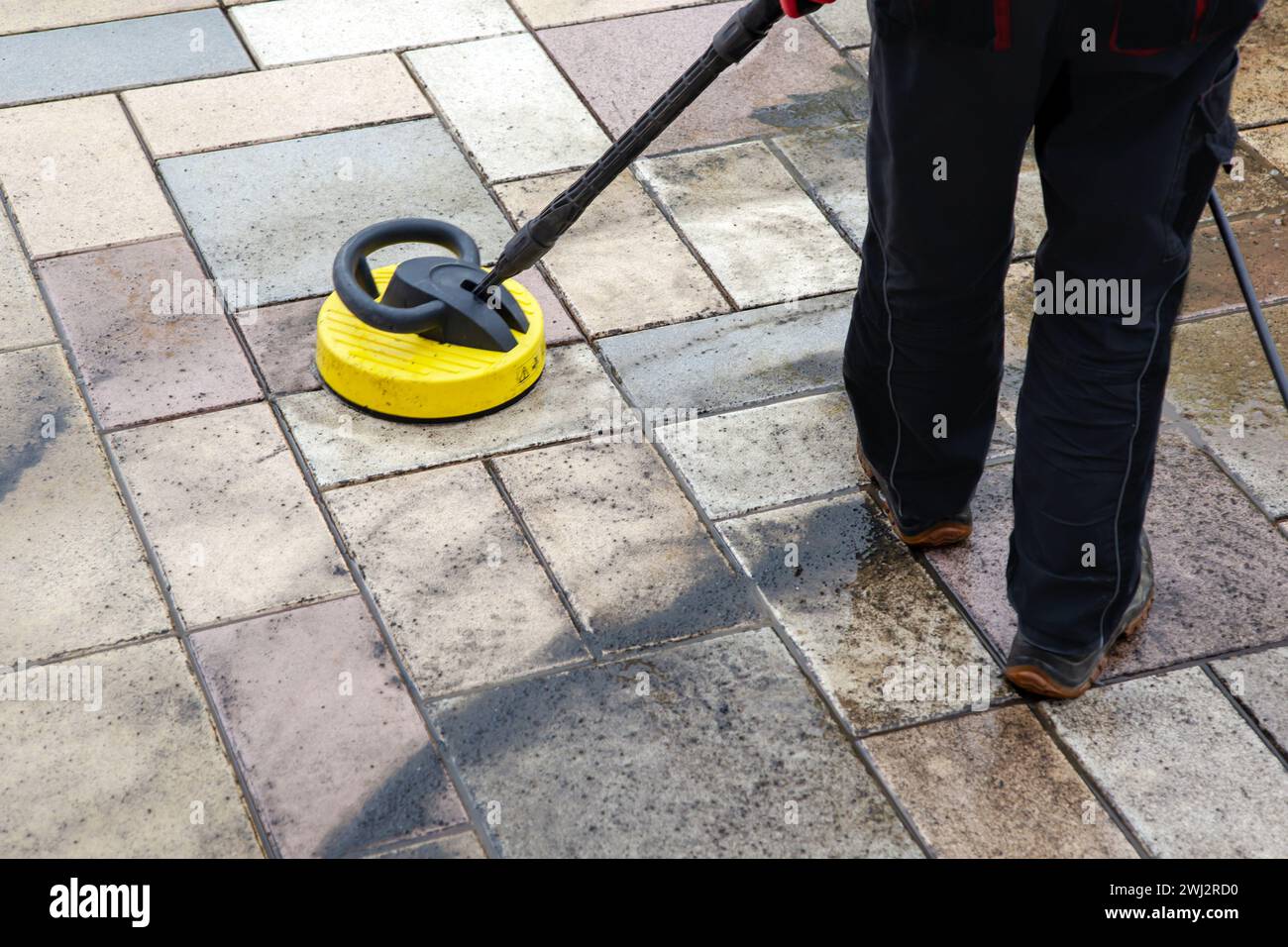 Cleaning stone slabs on patio with the highpressure cleaner. Person