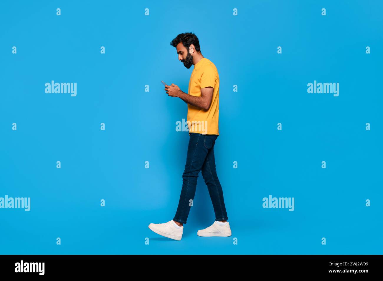 Middle aged indian man in yellow walking and texting on phone Stock Photo