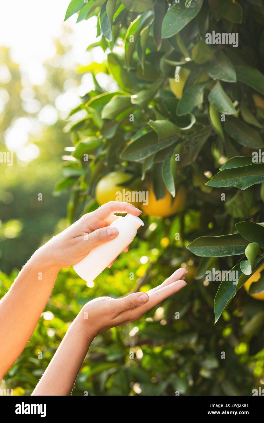 Woman holds bottle of skin care product in her hands on lemon tree background. Stock Photo