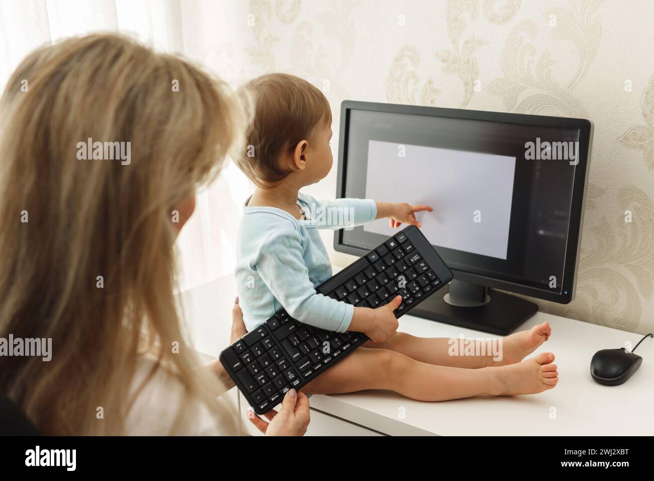 Little boy sitting on a desk and distracting mother from work on computer. Stock Photo