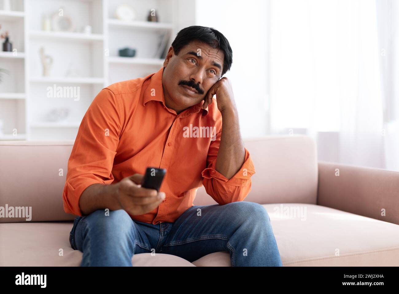 Unhappy mature eastern man sitting on couch, holding remote Stock Photo