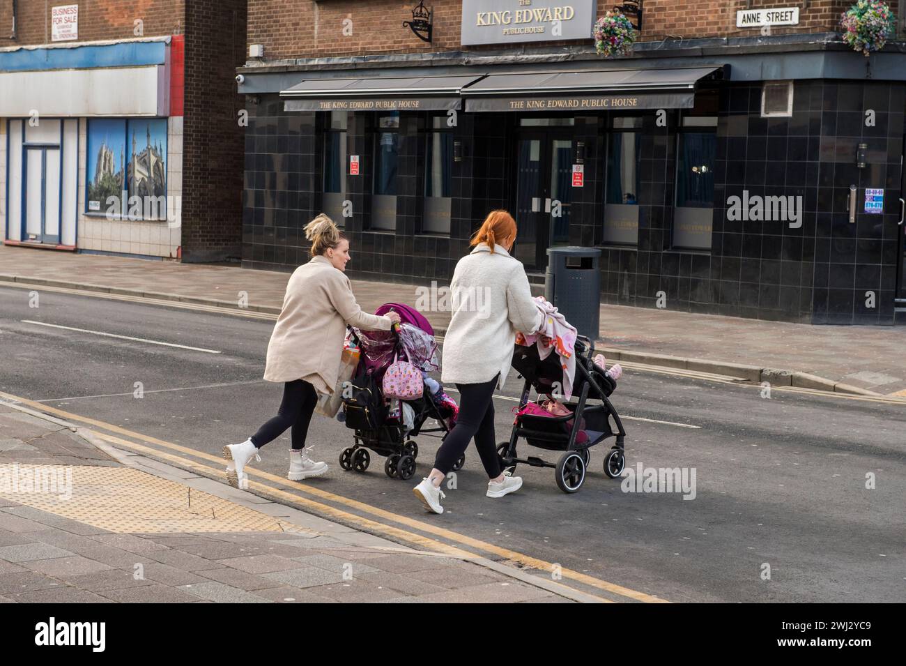 Two women pushing prams, cross a road towards a pub in Hull, East Yorkshire. Stock Photo