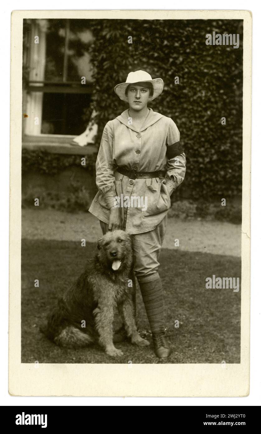 Original WW1 era postcard of a landgirl called Esme Greene wearing a beige tunic denoting general farm duties (as opposed to white uniform for dairying) and a 3 month service armband. She wears breeches, a knee-length overall tunic (with a belt). She is standing outside a country house or farm, with dog called Kim, dated 1917, Easton in Gordano, near Bristol, UK Stock Photo