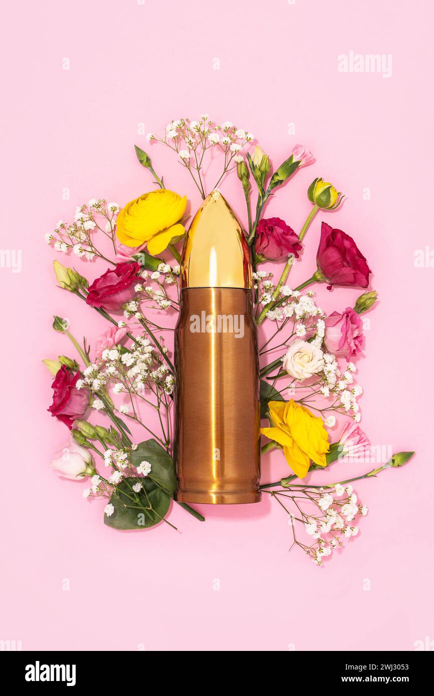 Pacifism and non-violence movement. Bullet and bunch of different flowers against pastel pink background. Stock Photo