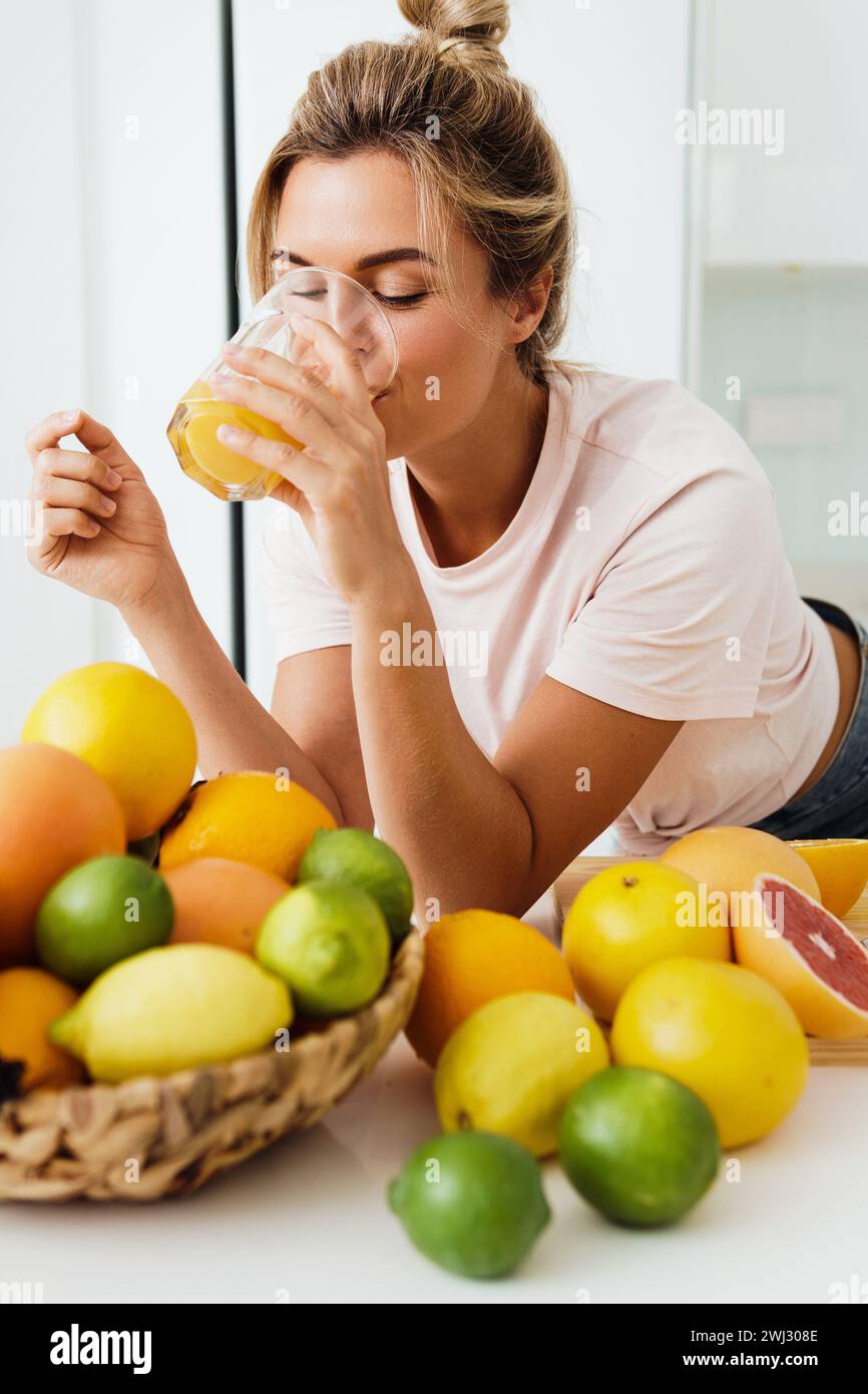 Woman drinking freshly squeezed homemade orange juice in white kitchen Stock Photo
