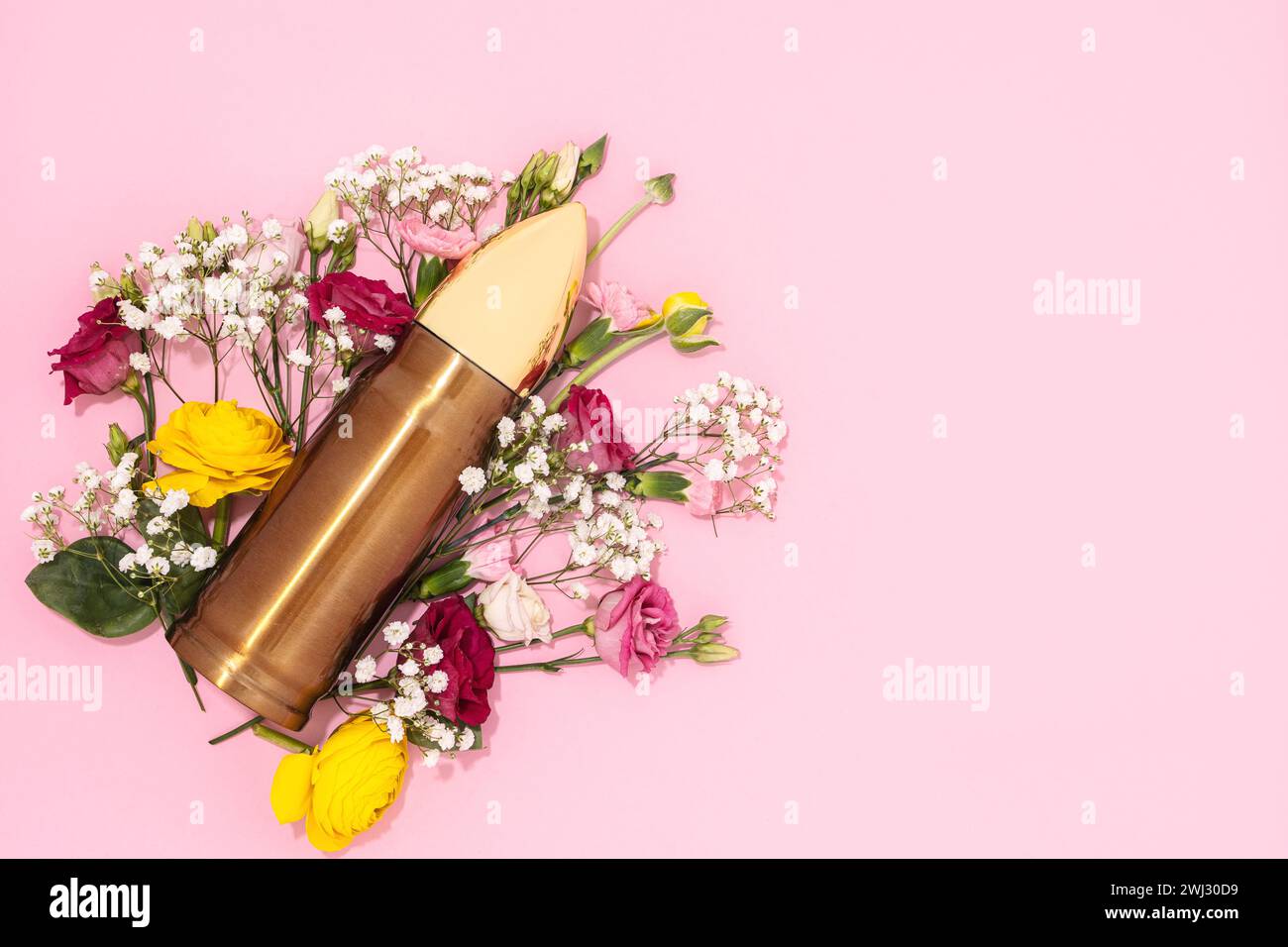 Pacifism and non-violence movement. Bullet and bunch of different flowers against pastel pink background. Stock Photo