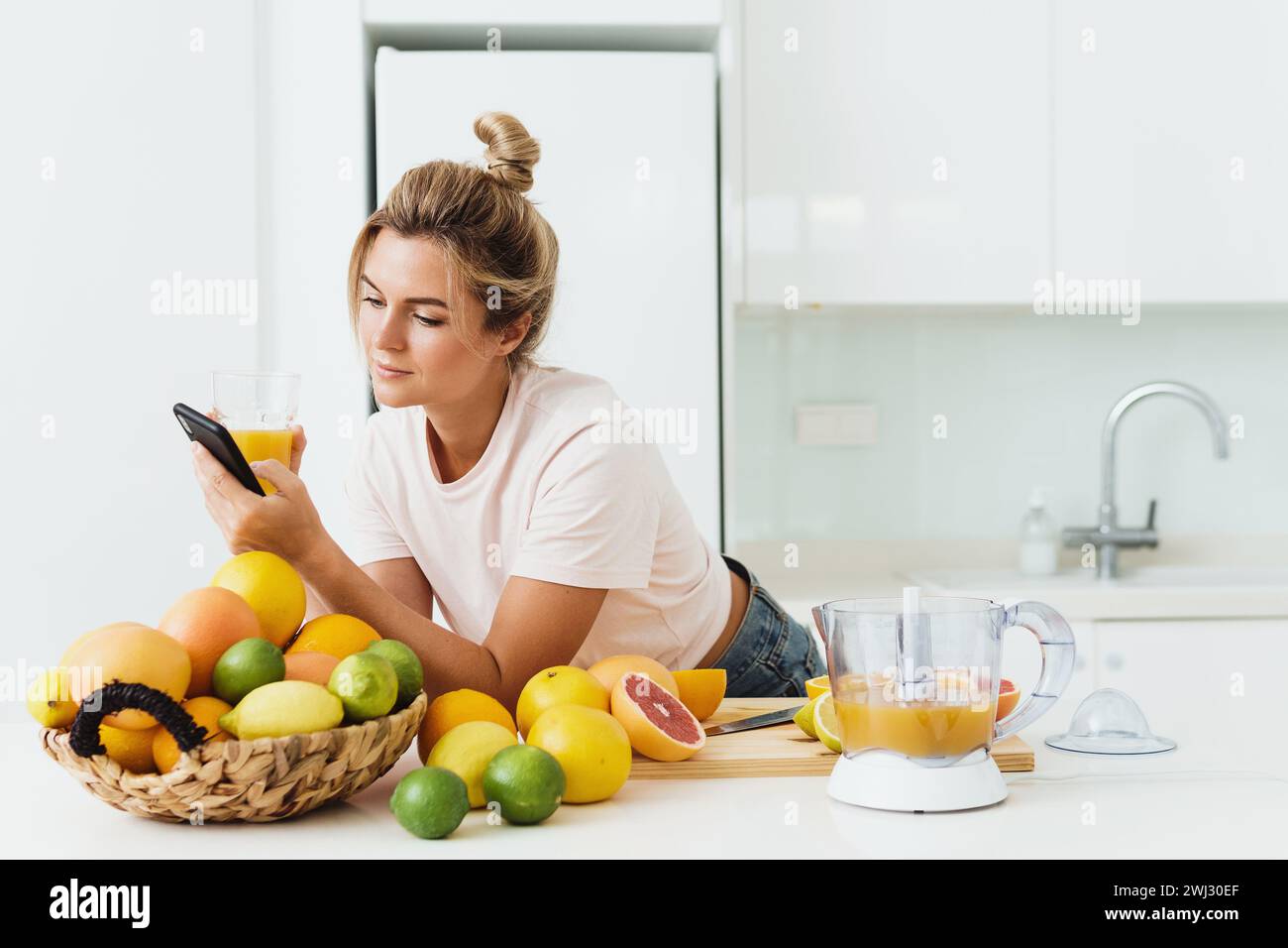 Young woman drinking freshly squeezed homemade orange juice and using smartphone Stock Photo