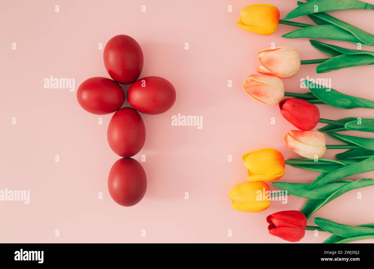 Creative Easter holiday composition of red Easter eggs in a shape of a cross and colorful tulips on pastel pink background. Minimal Easter concept. Stock Photo