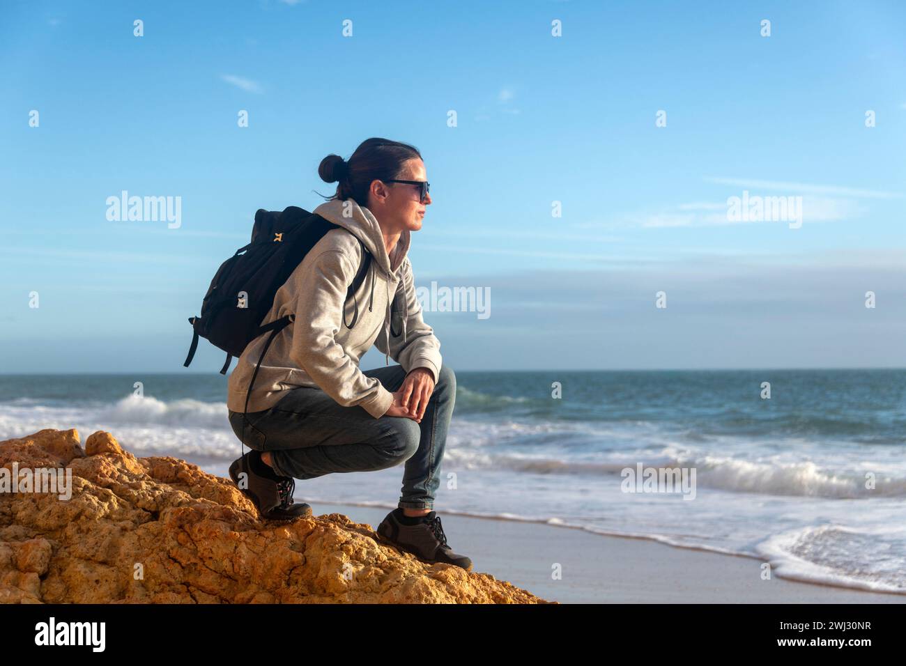 mid adult female walker crouching on rocks and looking at coastal view Stock Photo