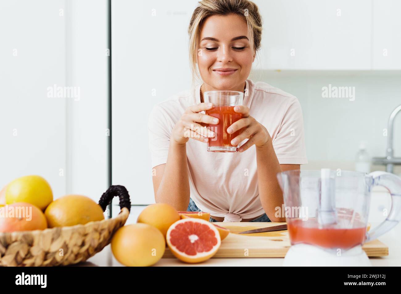 Woman drinking freshly squeezed homemade grapefruit juice in white kitchen Stock Photo