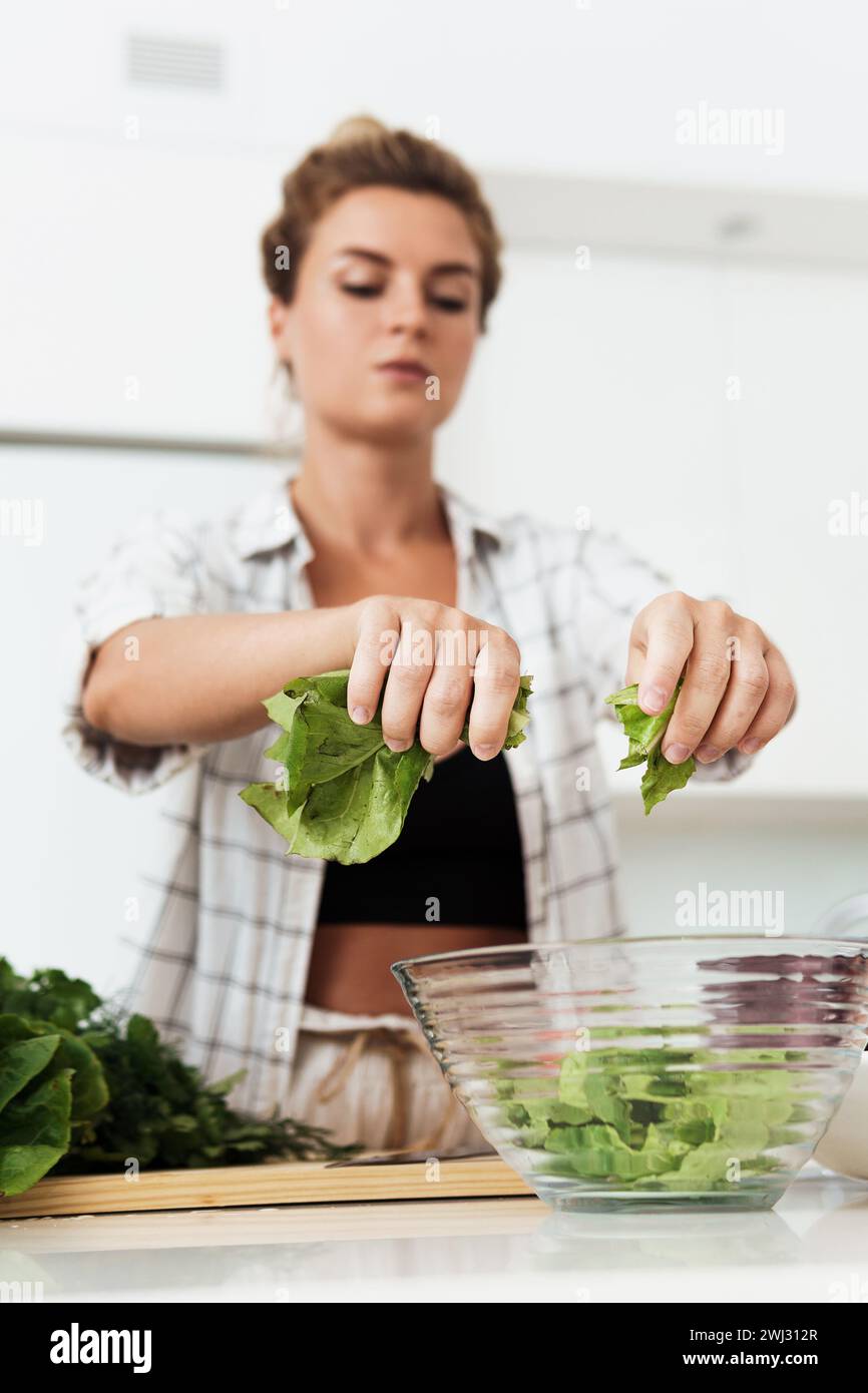 Young pretty woman tearing lettuce into bowl for salad Stock Photo
