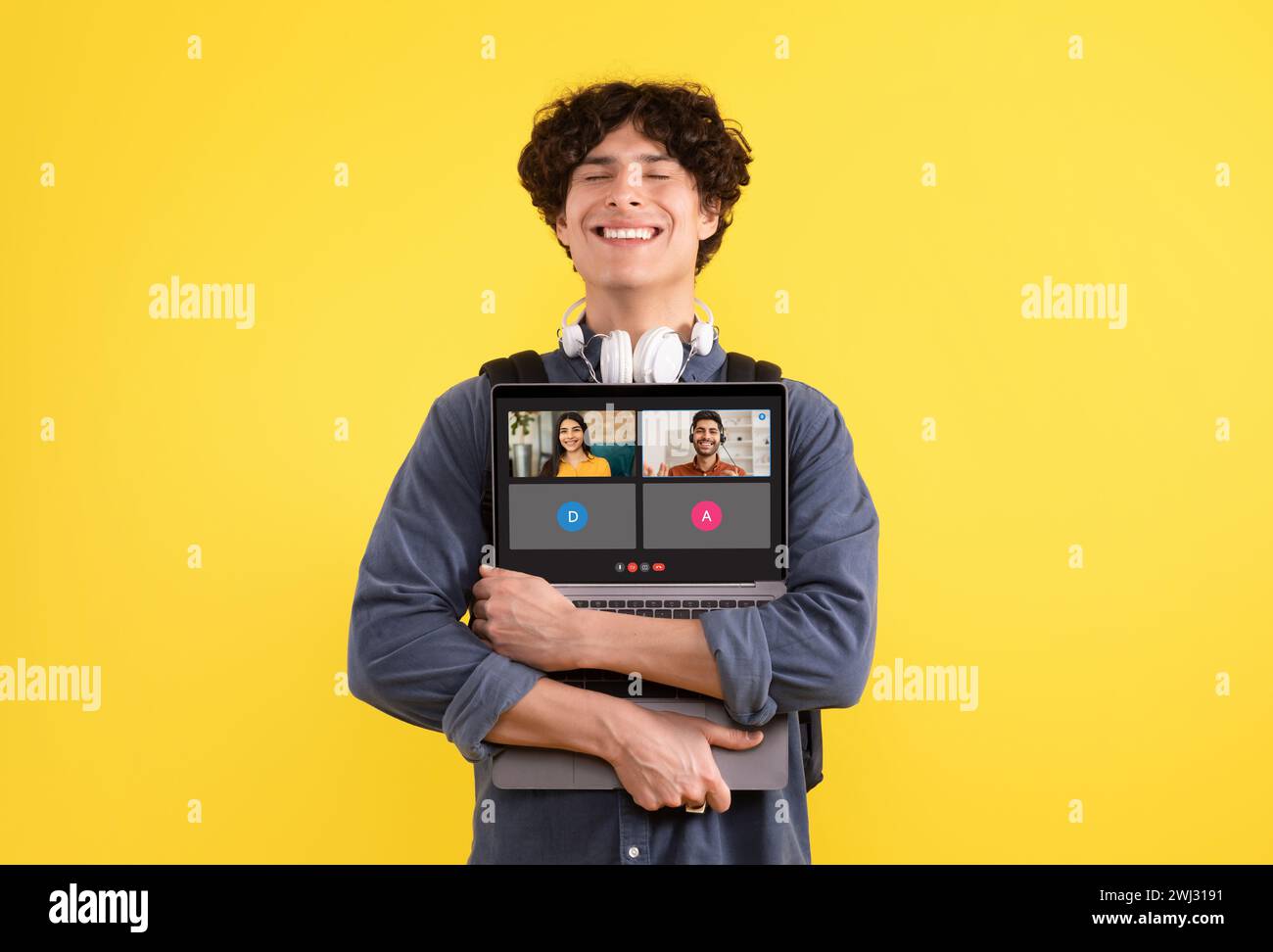 A young man with curly hair and headphones around his neck is smiling ...