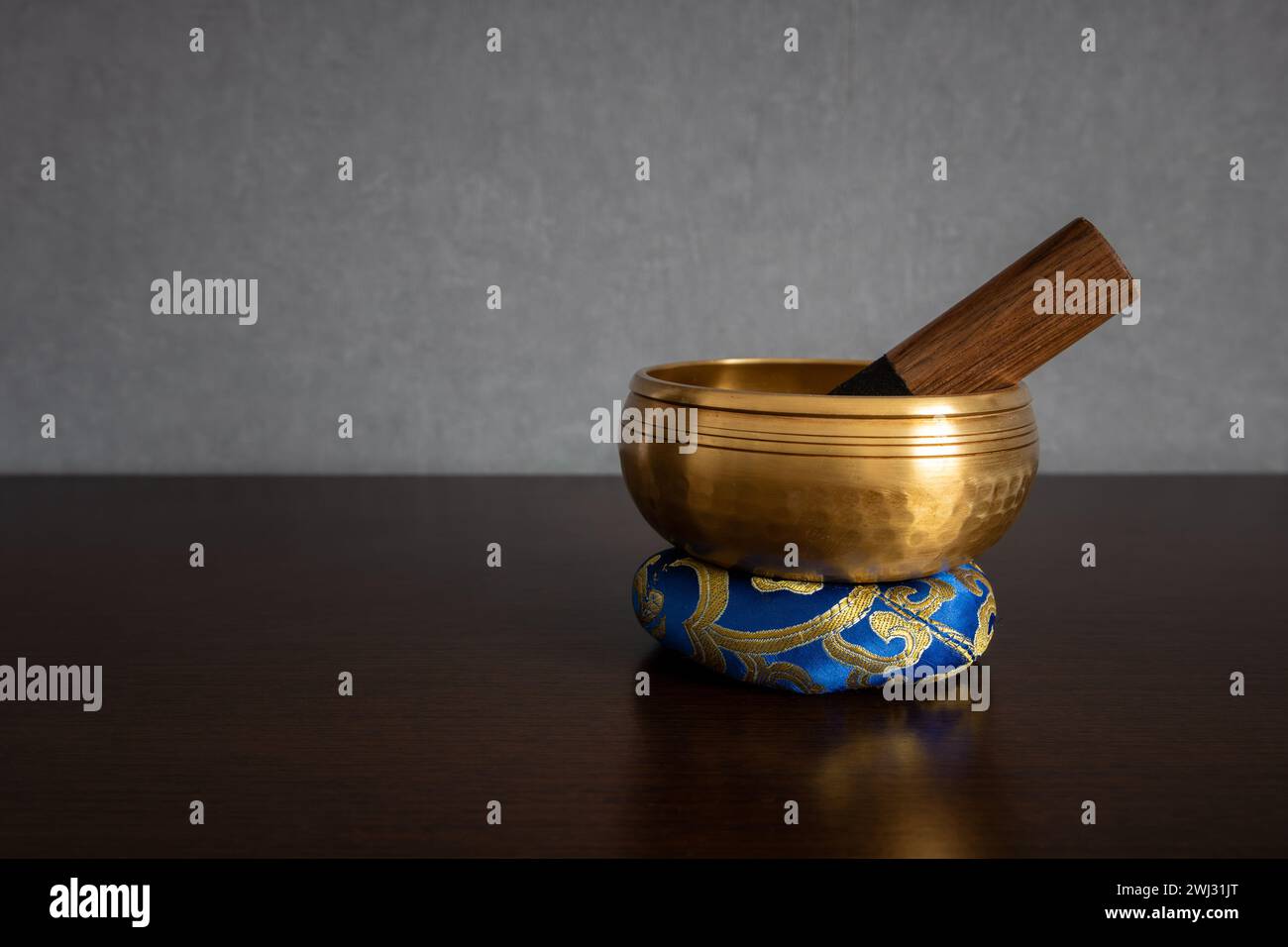 A golden colored Tibetan singing bowl with striker inside standing on a ring cushion isolated on a blurred clean background and empty space for text Stock Photo