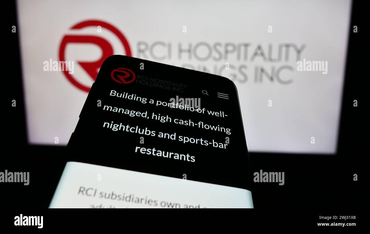 Mobile phone with website of US nightclub company RCI Hospitality Holdings Inc. in front of business logo. Focus on top-left of phone display. Stock Photo