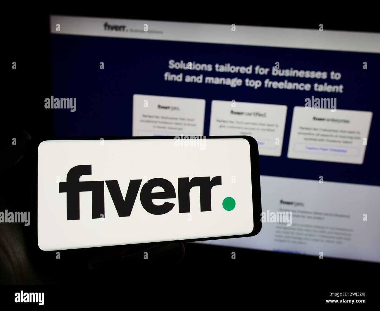 Person holding mobile phone with logo of freelance platform company Fiverr International Ltd. in front of web page. Focus on phone display. Stock Photo